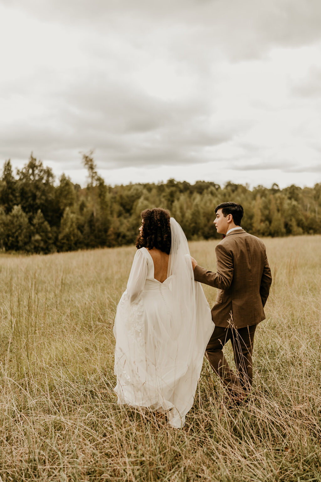 A bride and groom walking through the grass.