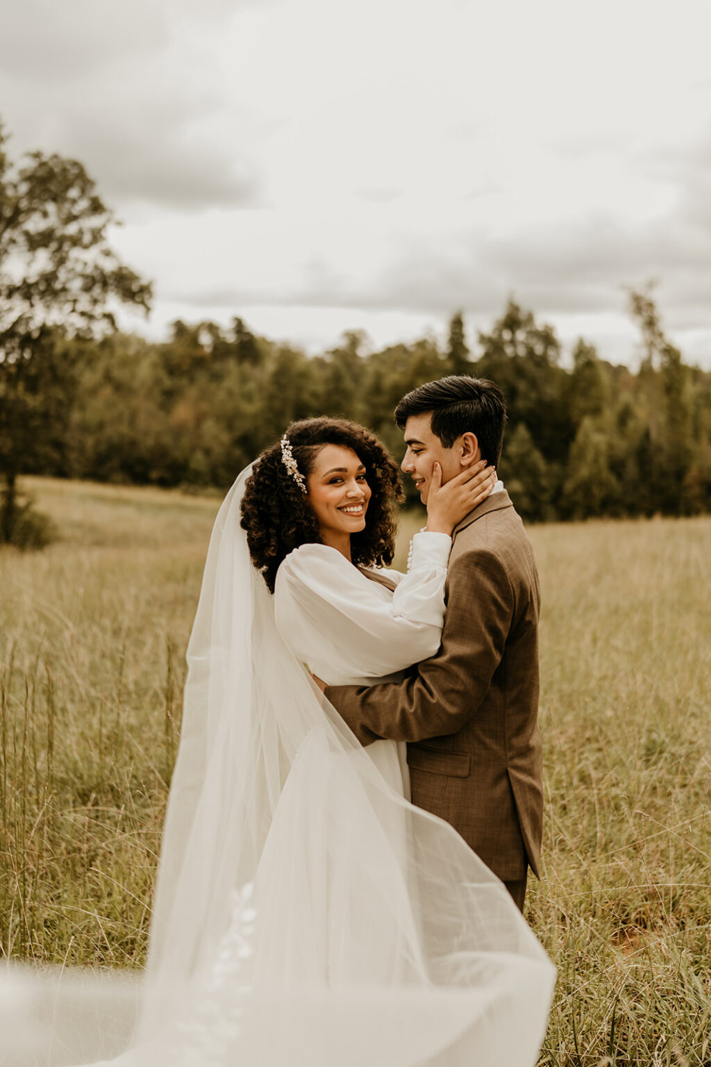 A bride and groom embracing in the middle of a field.