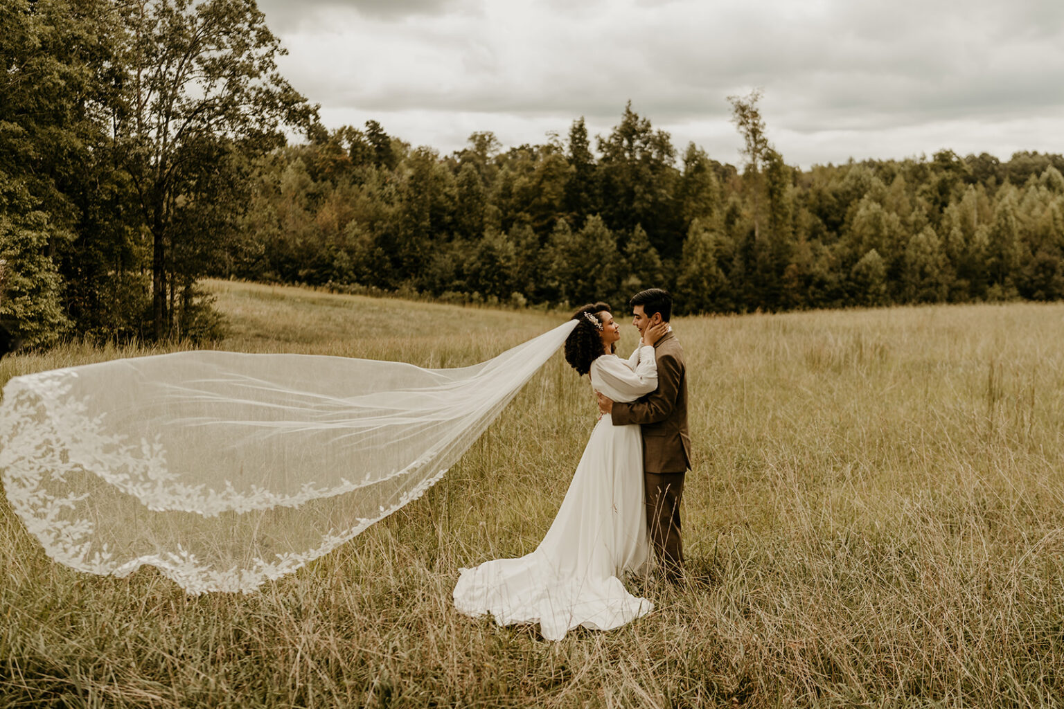 A couple is kissing in the grass with trees in the background.