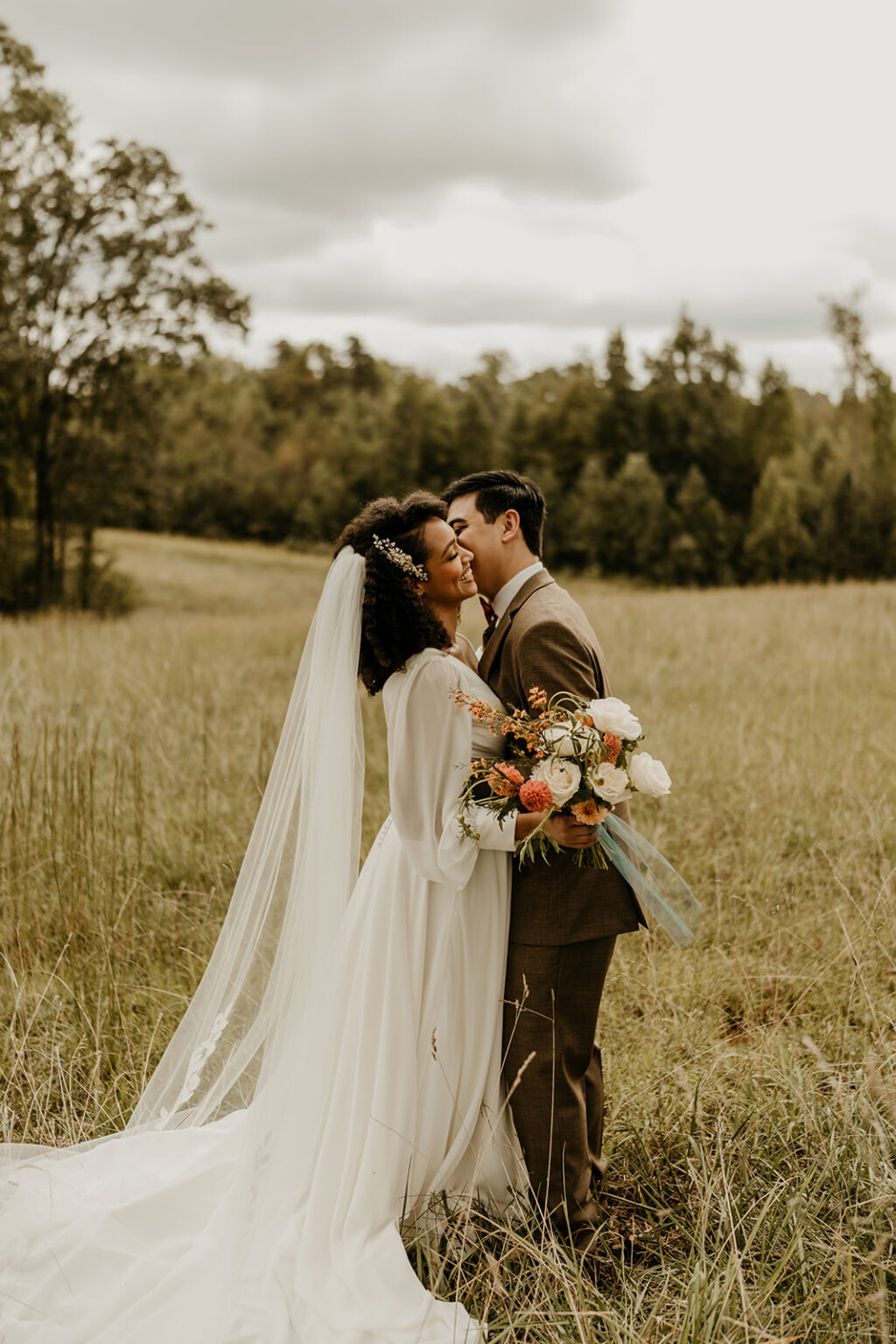 A bride and groom kissing in the middle of a field.