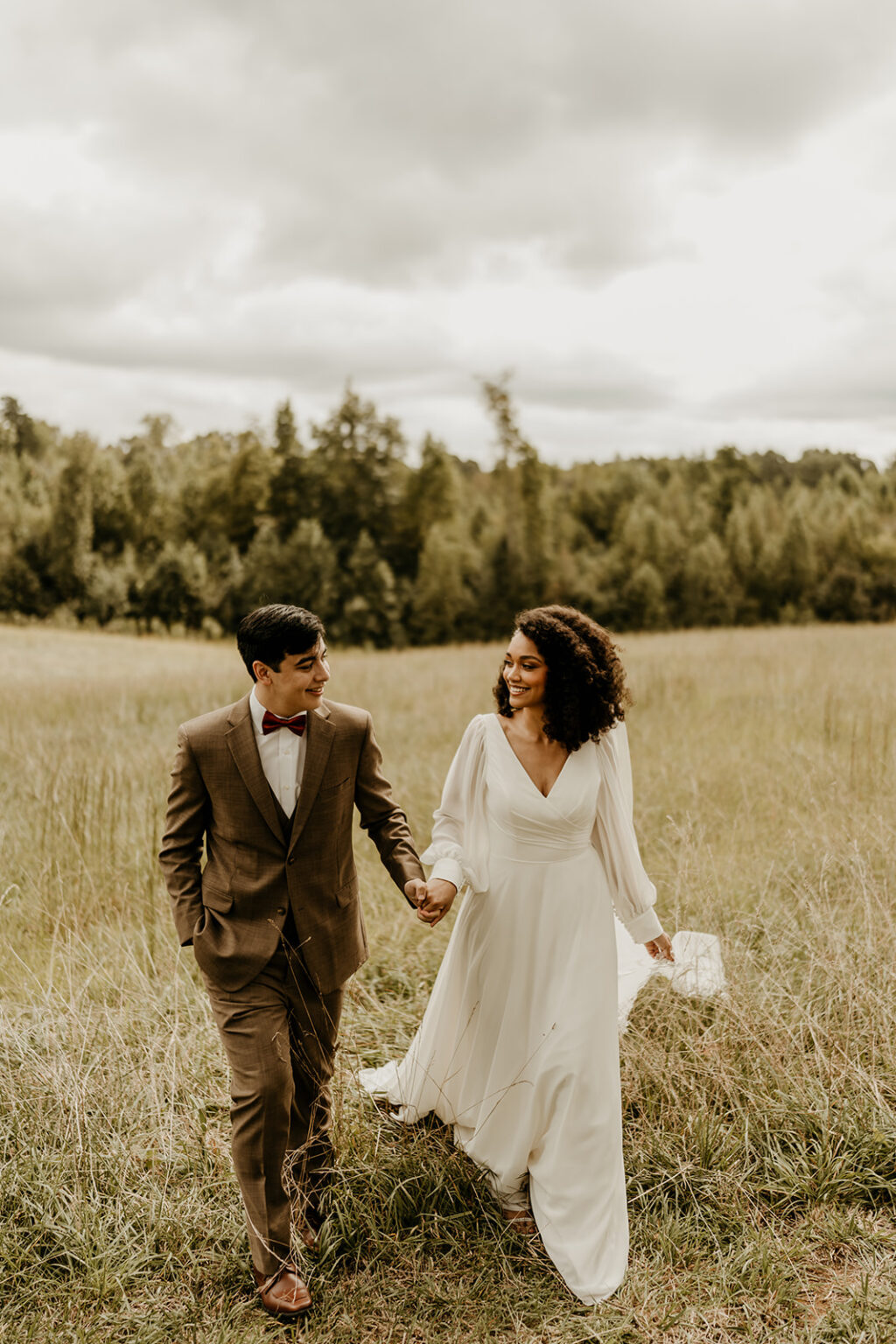 A man and woman holding hands while walking through the grass.