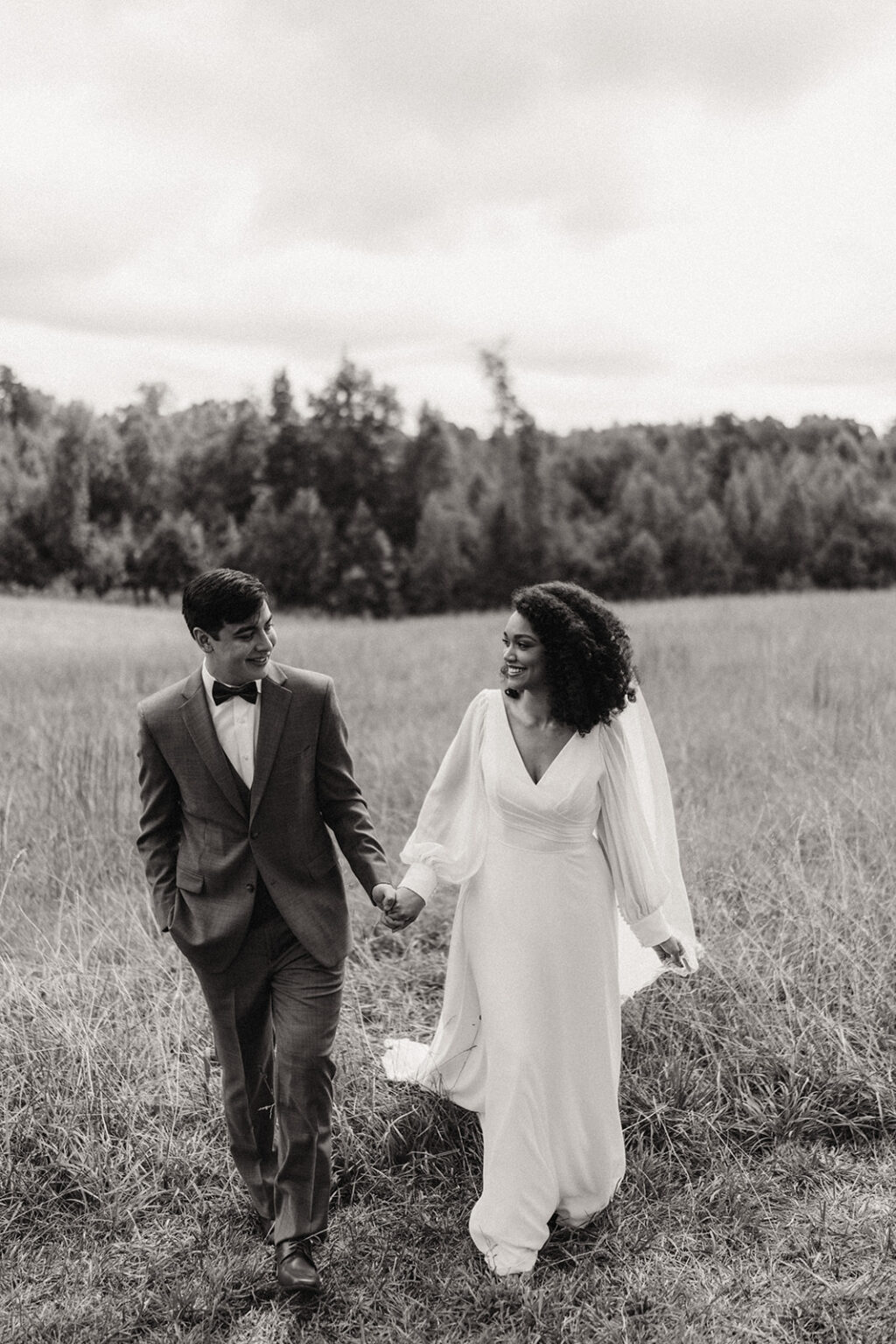 A man and woman holding hands while walking through the grass.