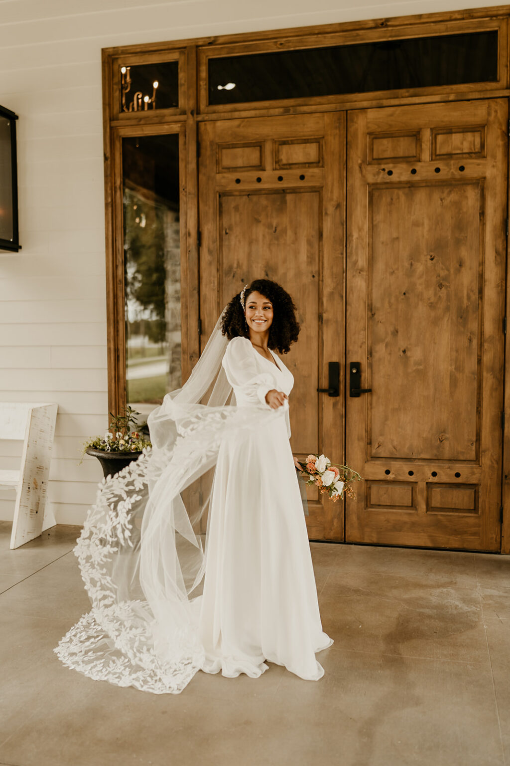 A woman in white dress standing next to wooden doors.