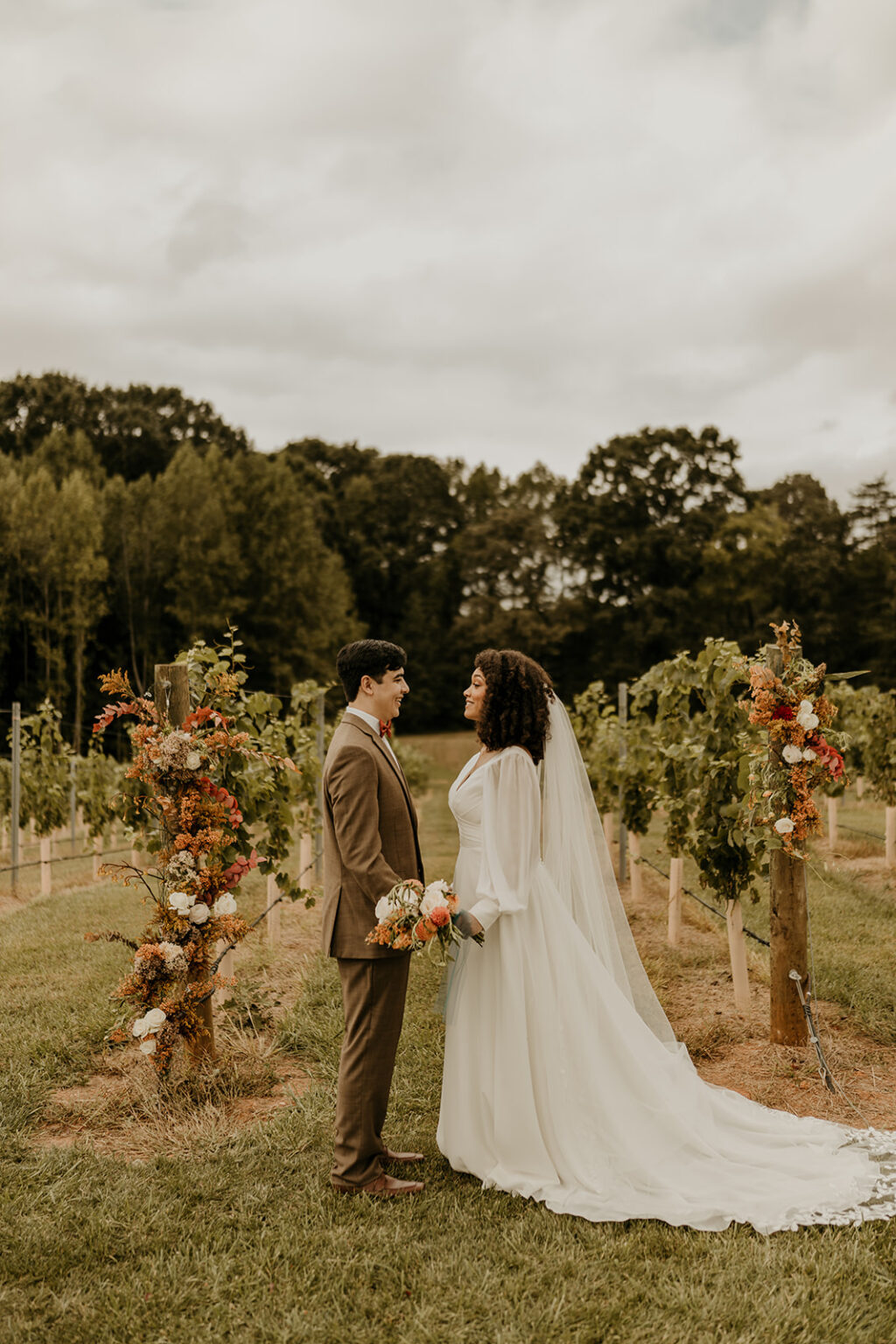 A couple standing in the middle of a vineyard.