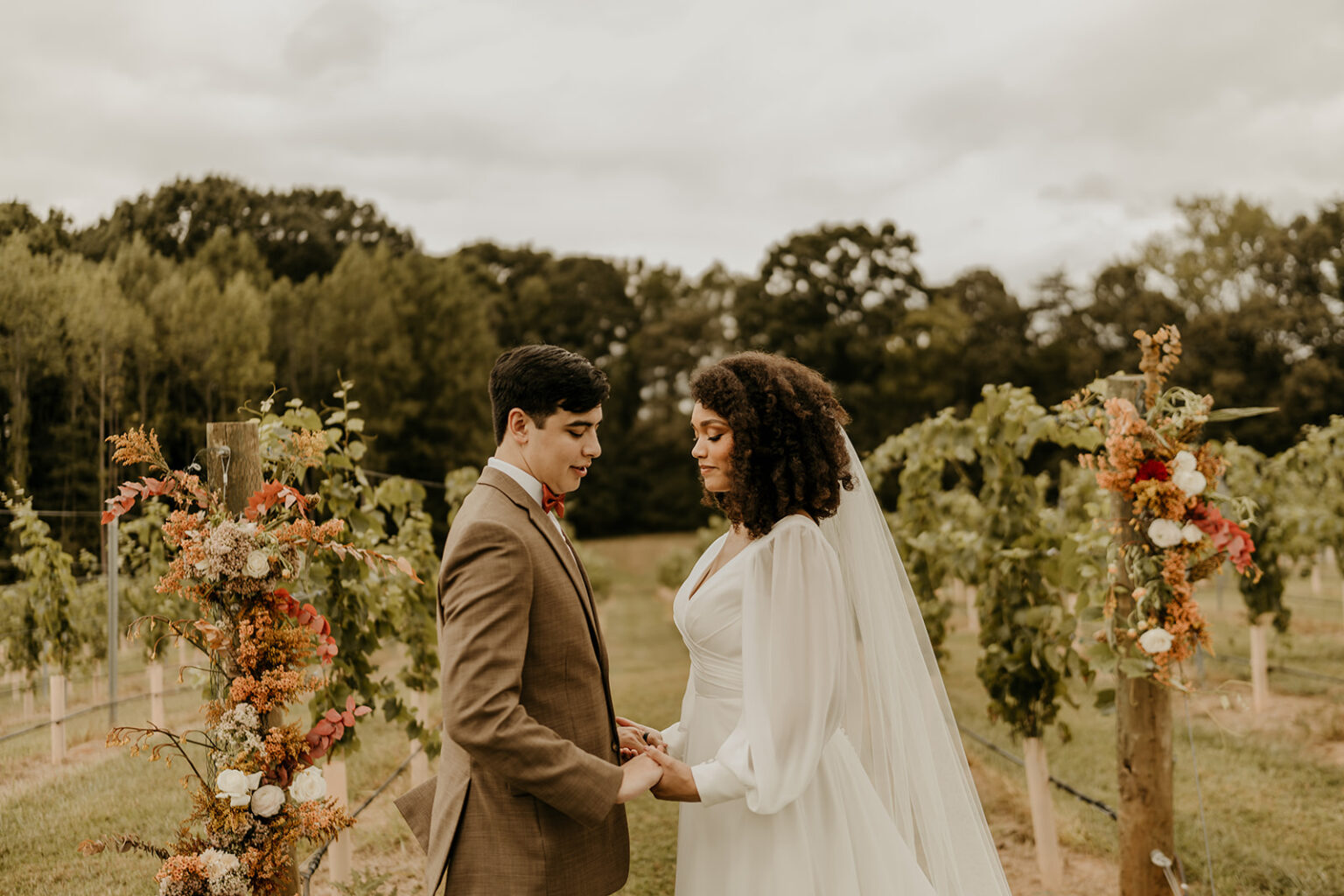 A man and woman holding hands in front of some vines.