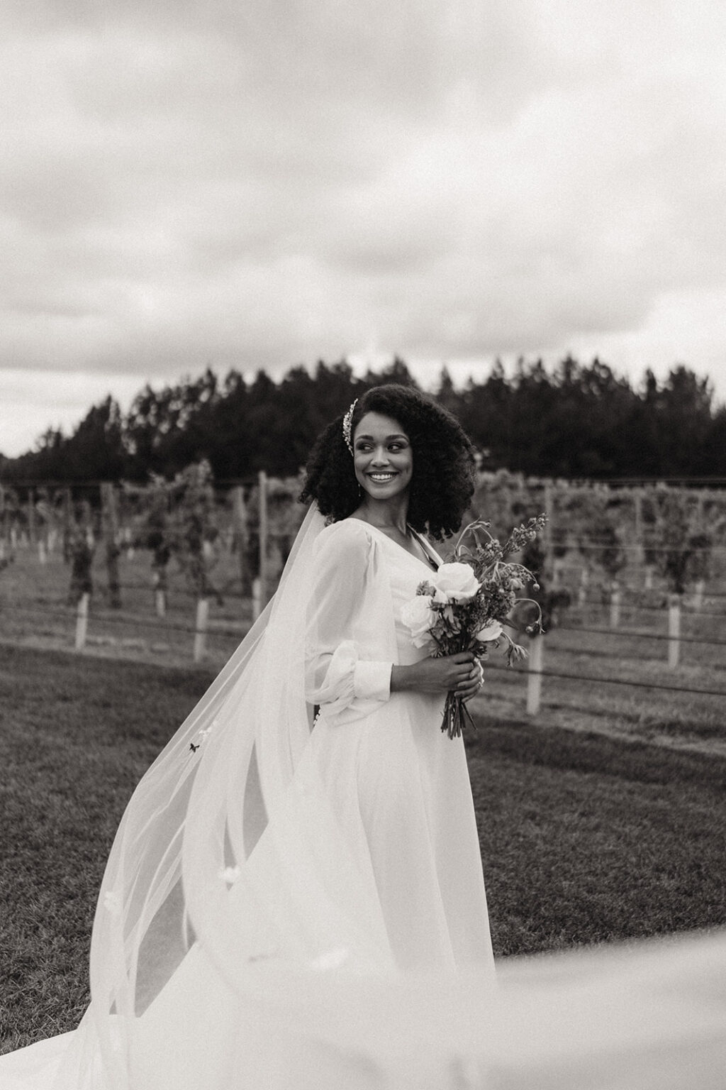 A woman in white dress holding flowers and smiling.