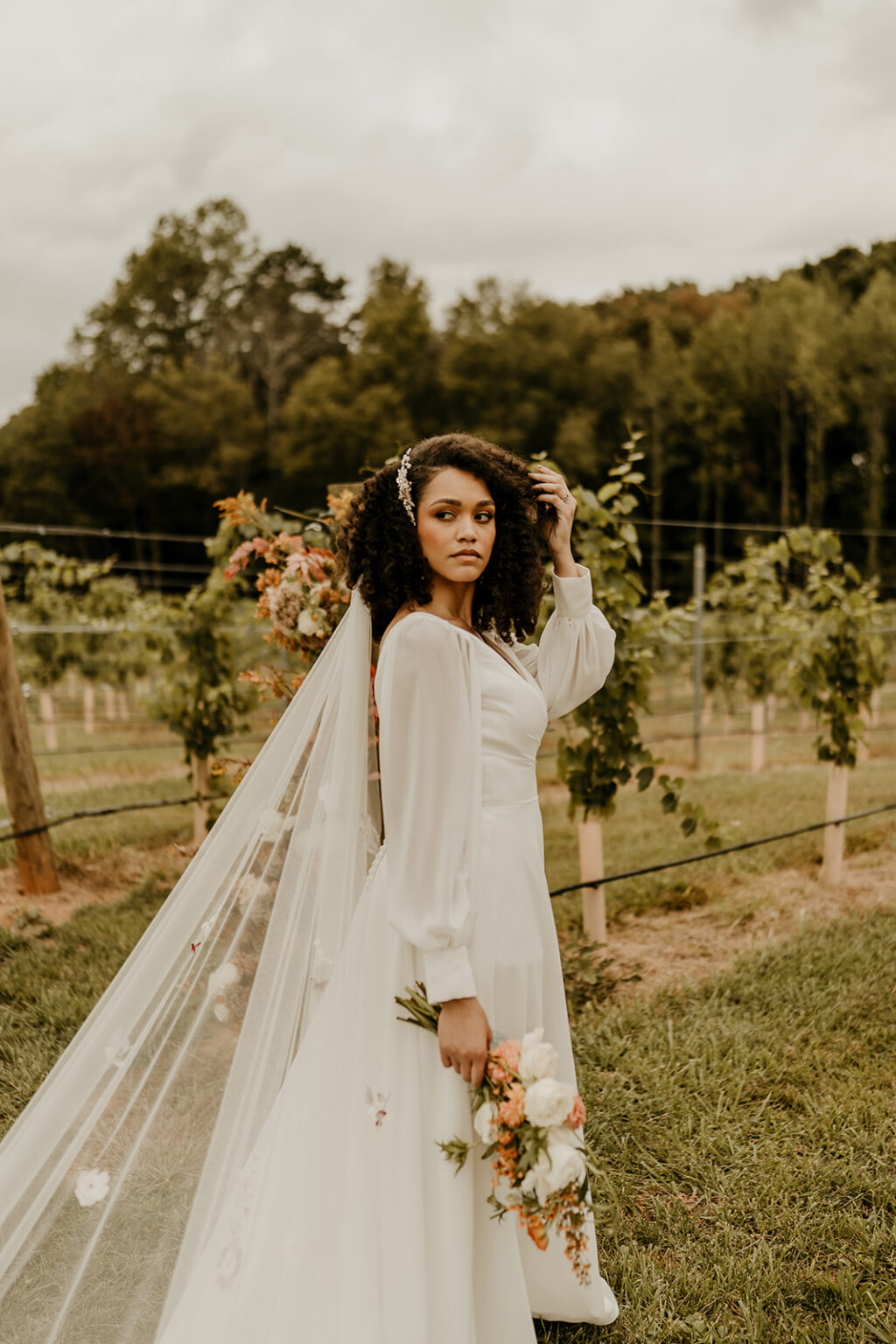 A woman in white dress holding flowers near fence.