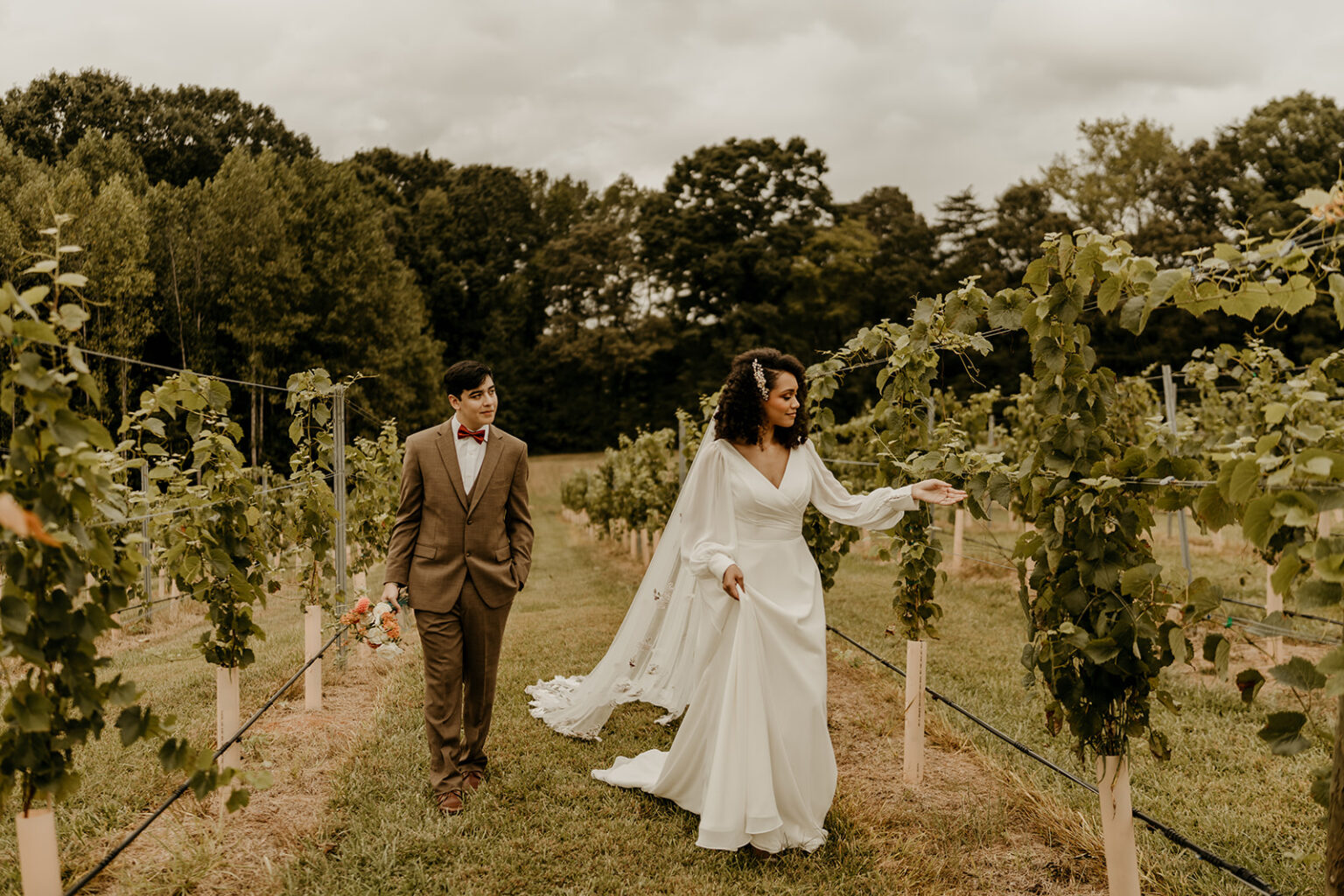 A bride and groom walking through the vines