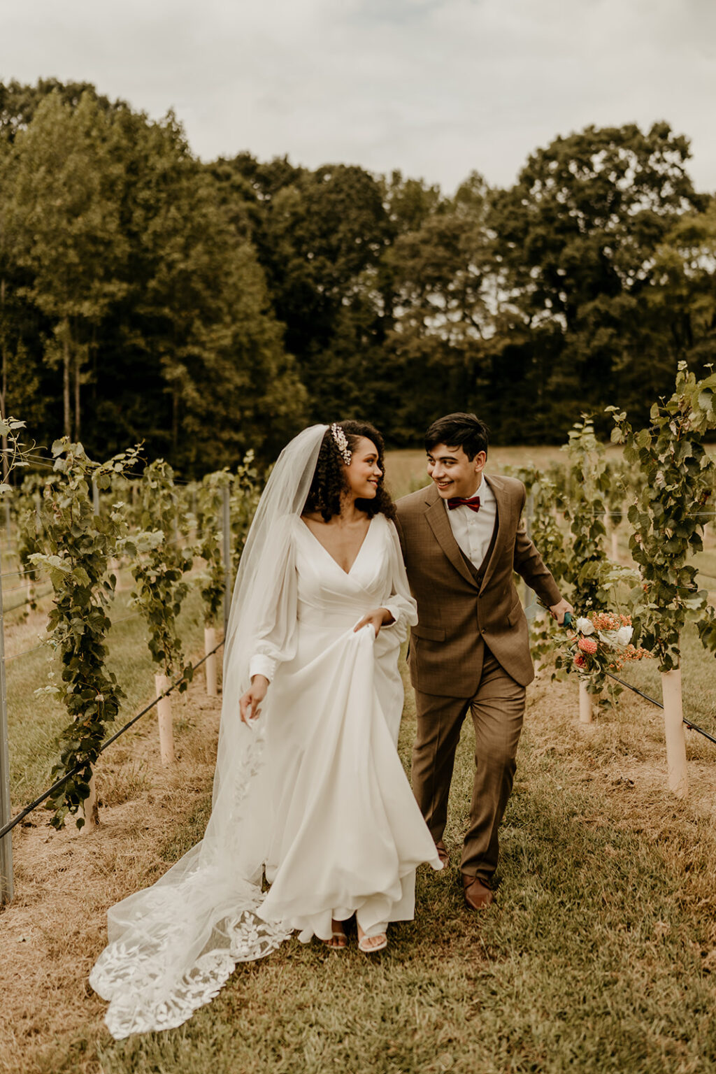 A bride and groom walking through the vines