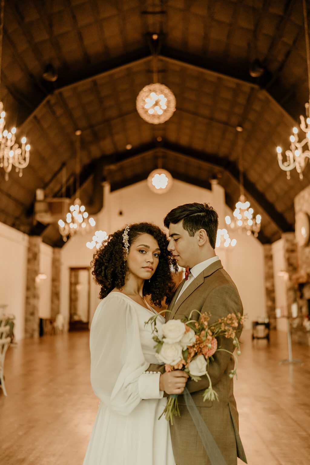 A man and woman holding flowers in front of a chandelier.