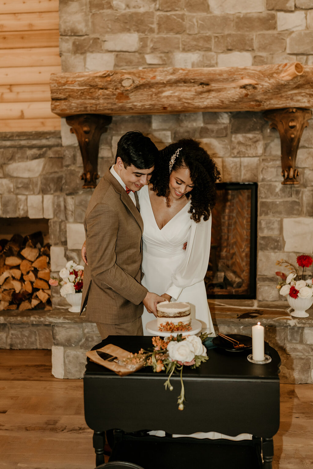 A couple cutting their wedding cake in front of the fireplace.