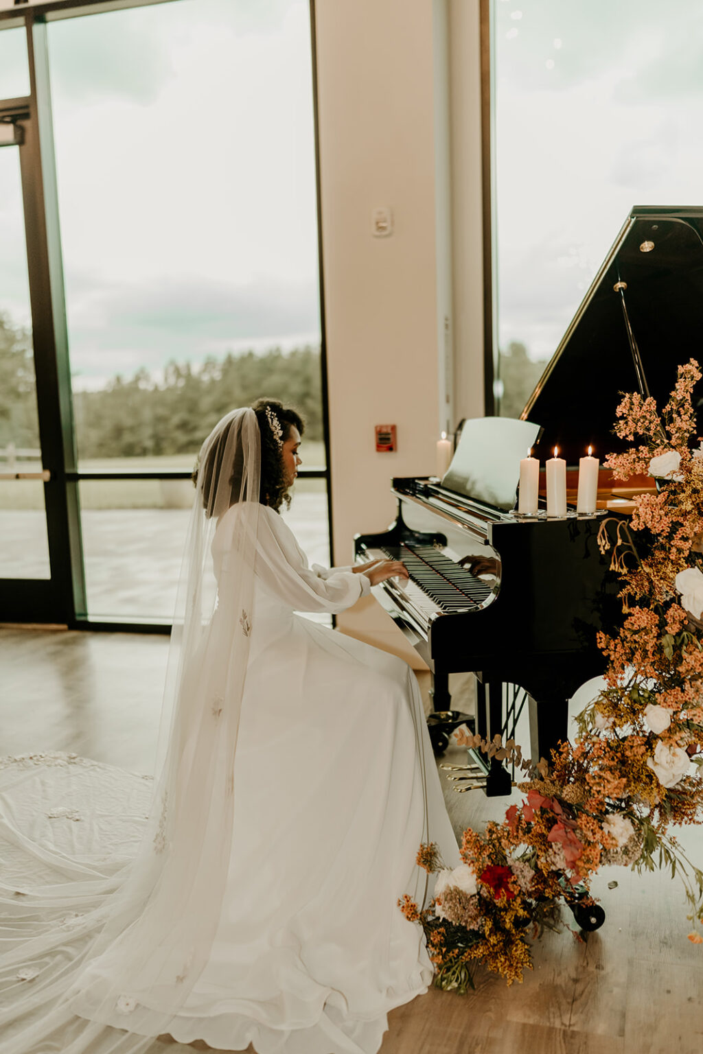 A woman in white dress playing piano near a christmas tree.