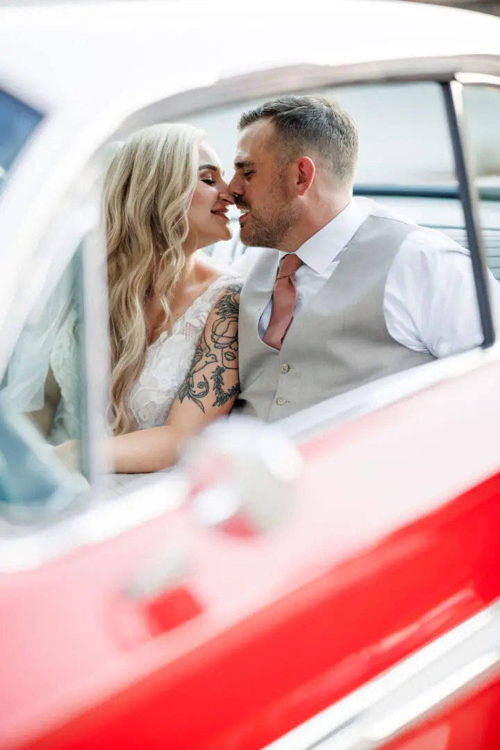 A bride and groom kissing in the back of a car.