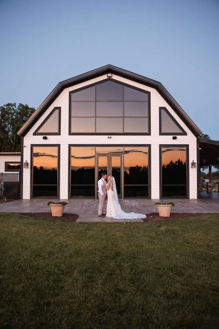 A bride and groom pose for the camera outside of their barn.