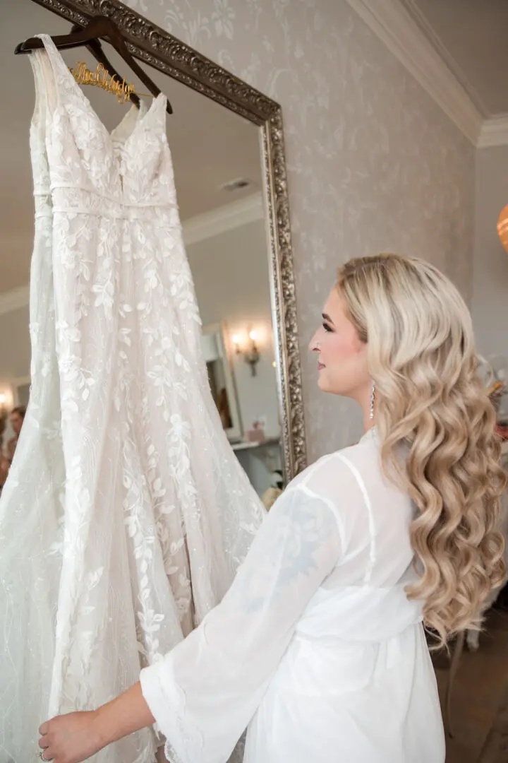 A woman looking at a wedding dress hanging in the mirror.