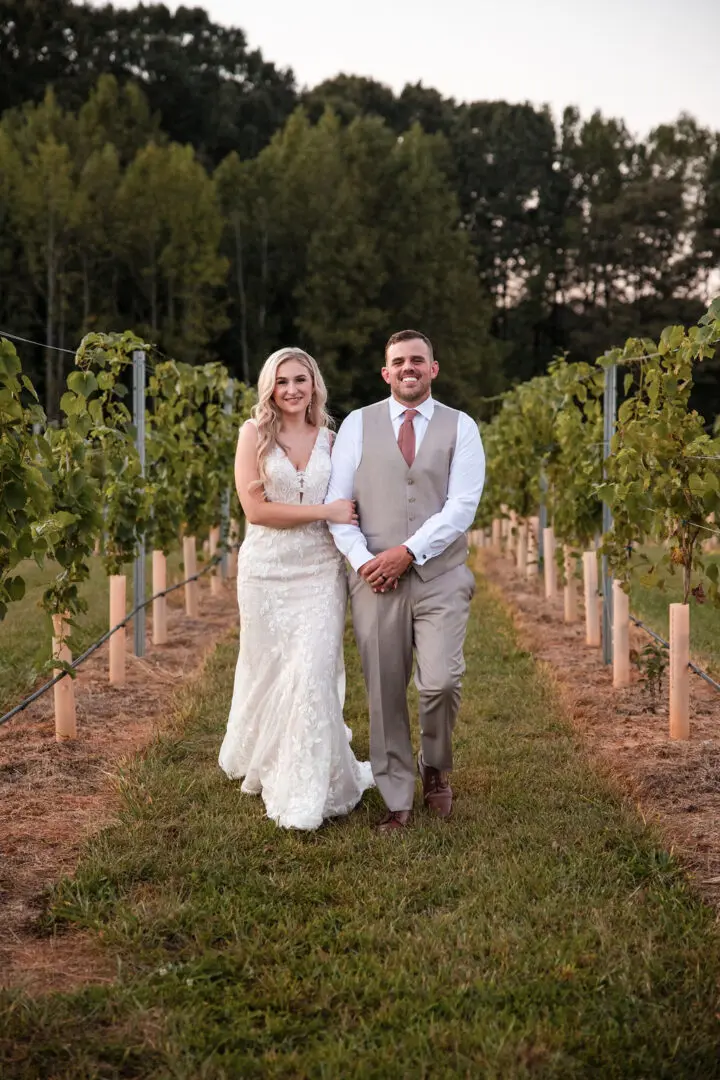 A man and woman posing for a picture in the middle of a vineyard.