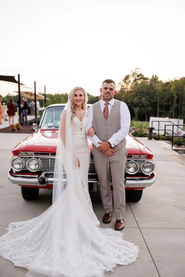 A bride and groom standing in front of an old car.