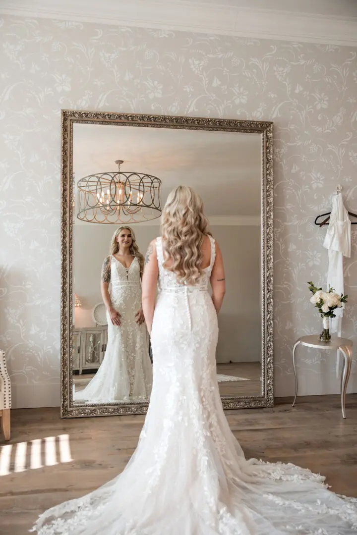 A woman in a white dress standing next to a mirror.