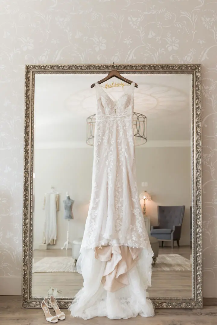 A wedding dress hanging up in front of a mirror.