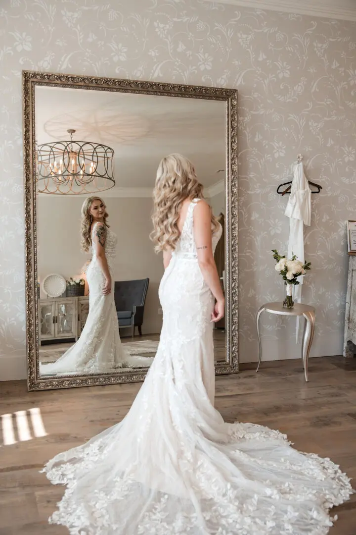 A woman in a wedding dress standing next to a mirror.