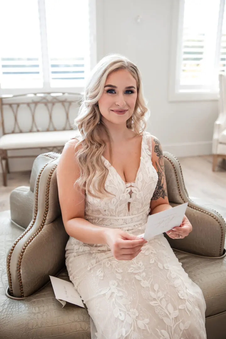 A woman in white dress sitting on chair holding paper.