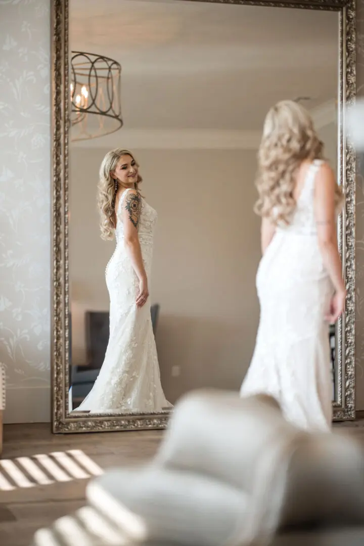 A woman in white dress standing next to a mirror.