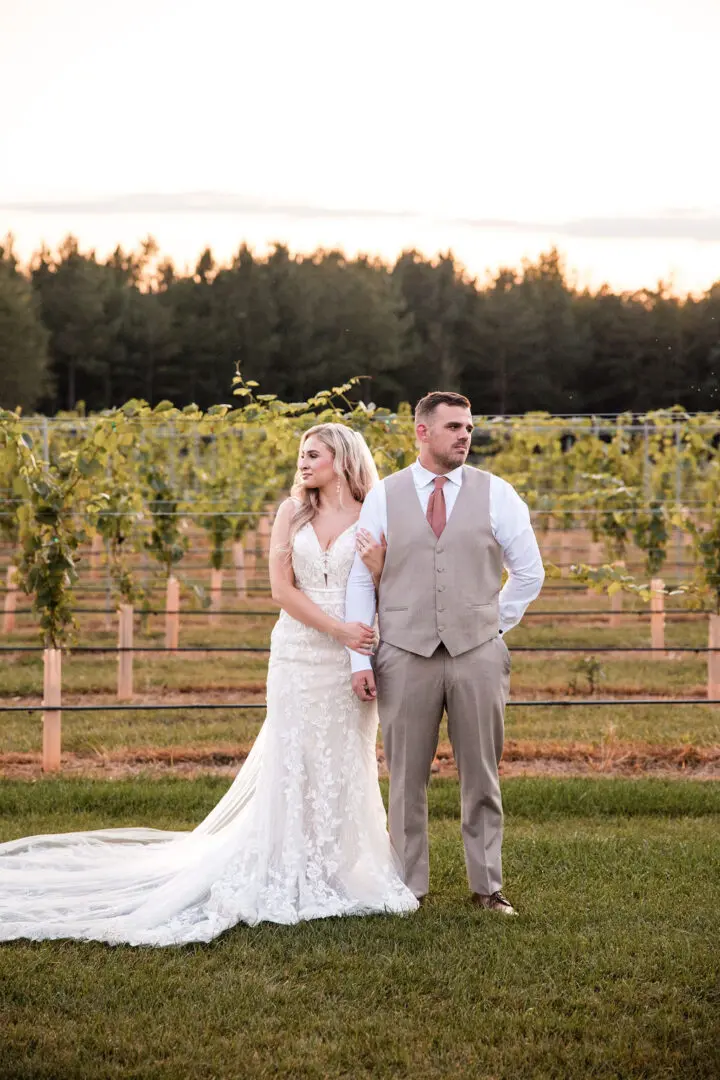 A bride and groom pose for a picture in front of some vines.