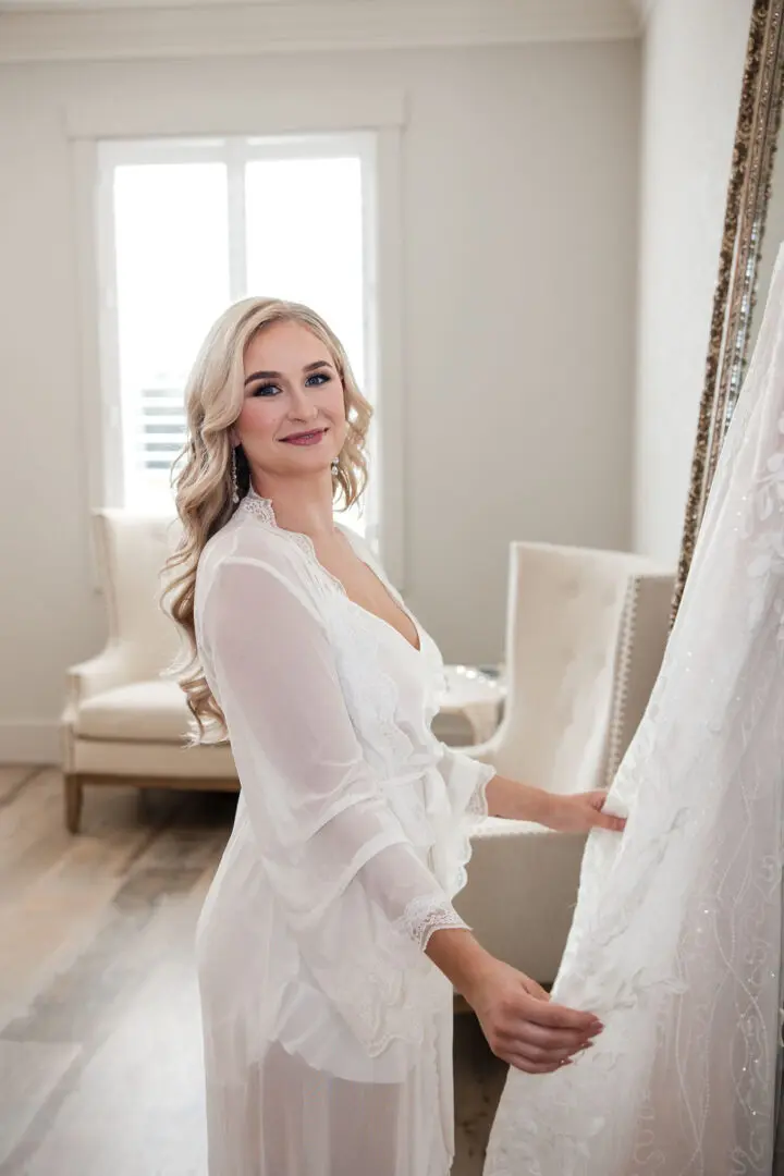 A woman in white dress standing next to a curtain.