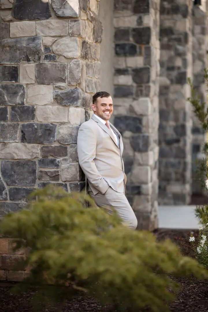 A man in suit and tie leaning against a stone wall.