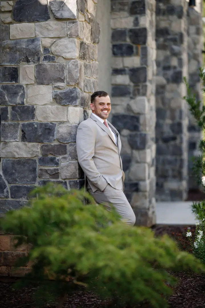 A man in suit leaning against a stone wall.