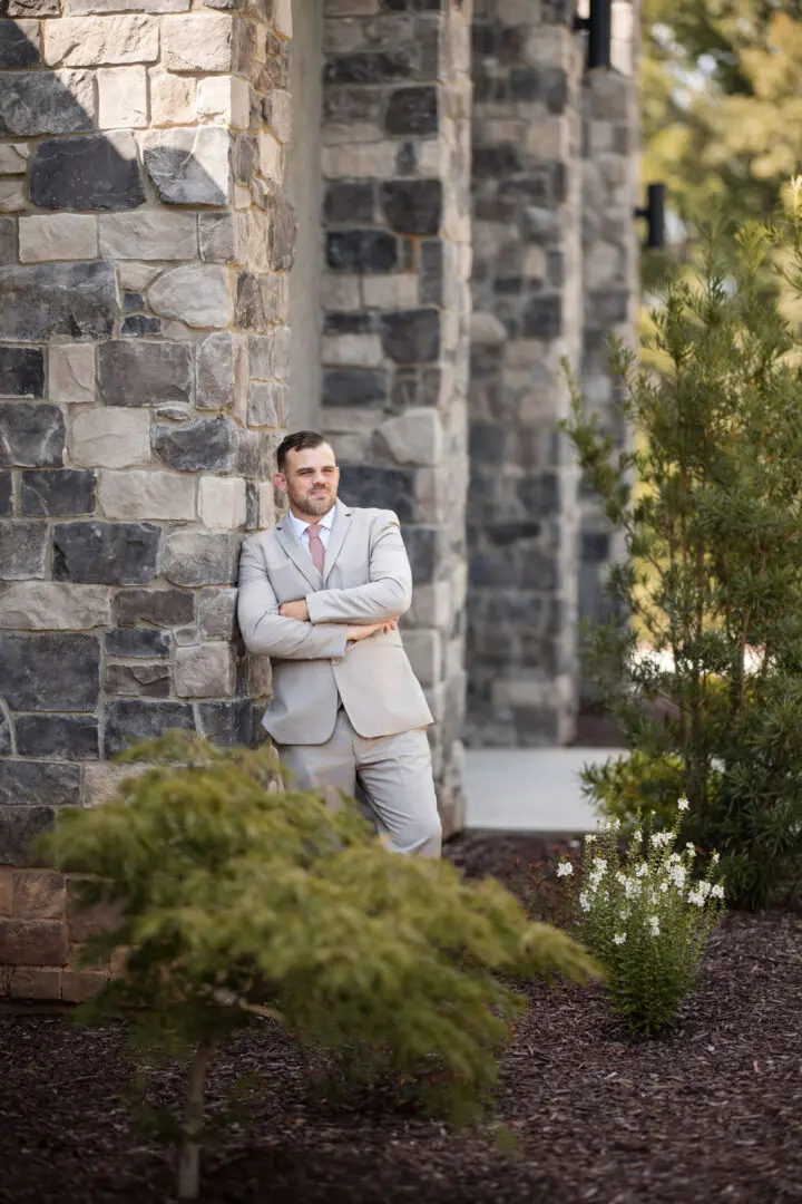 A man in suit and tie leaning against a stone wall.