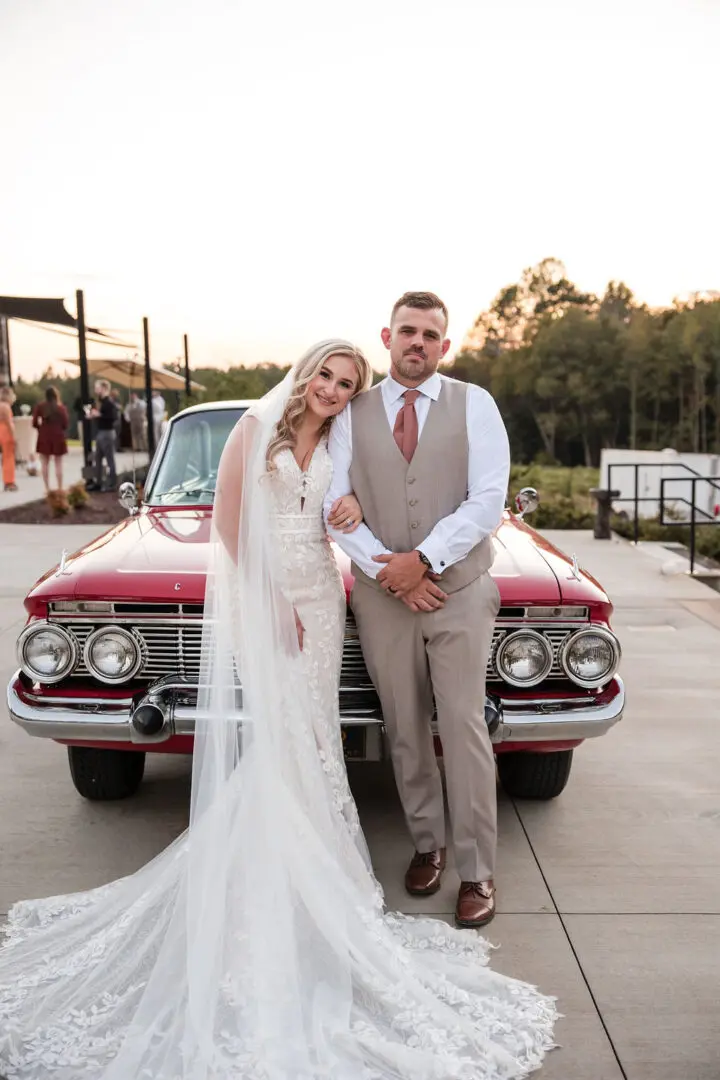 A bride and groom standing next to a red car.