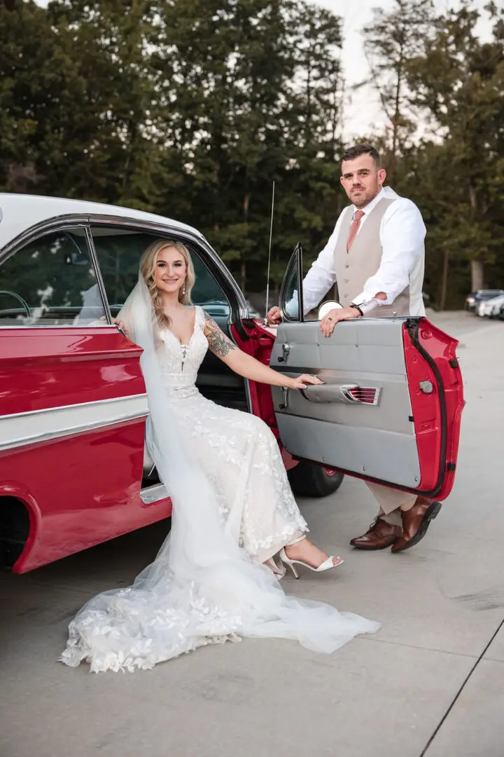 A bride and groom pose in the back of their car.