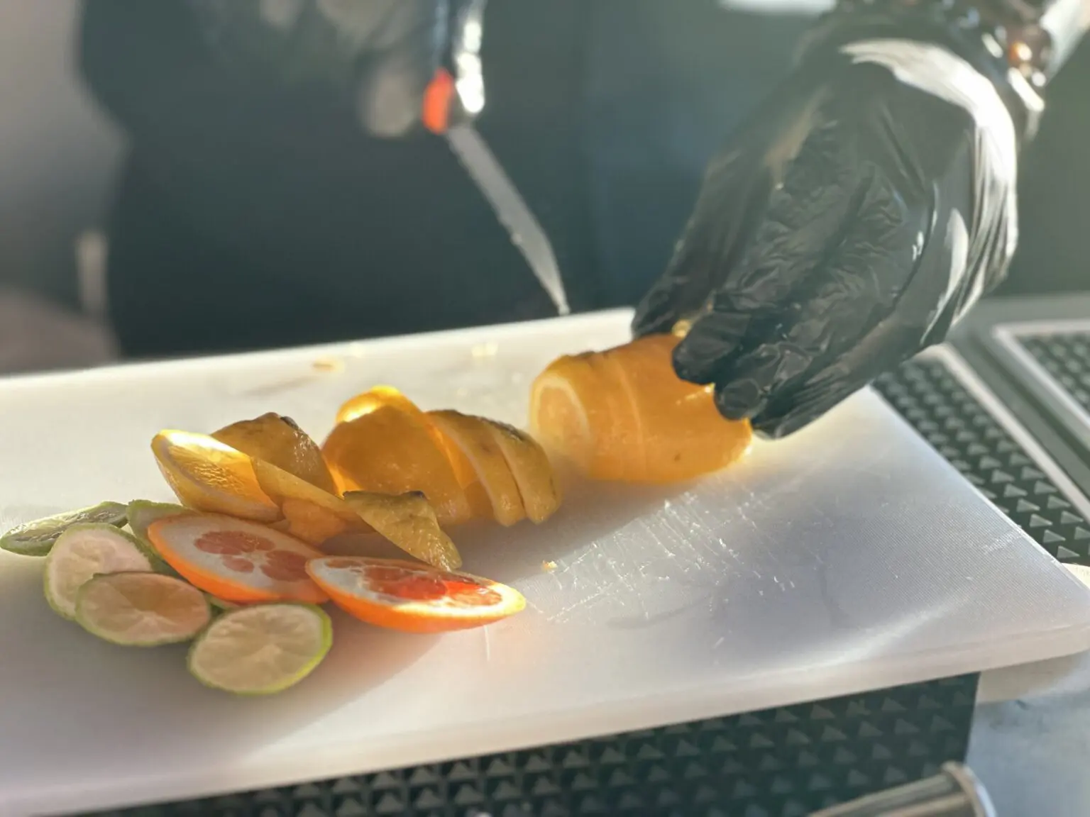 A person wearing black gloves cutting up fruit.