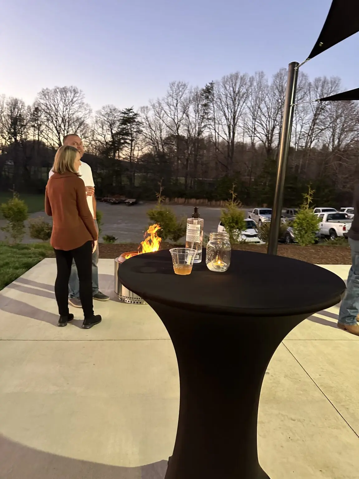 A woman standing next to an outdoor table with drinks on it.