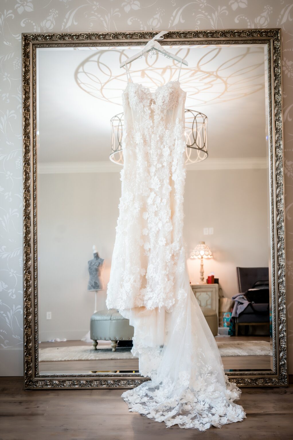 A wedding dress hanging in front of a mirror.